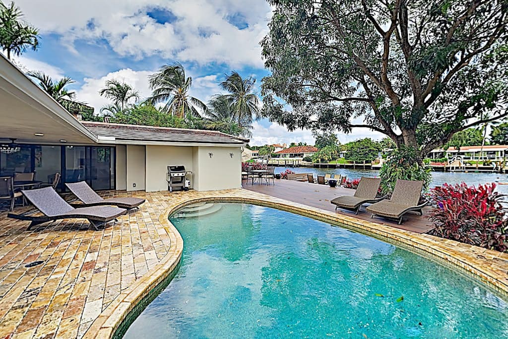 A pool deck with loungers and palms at a Fort Lauderdale home, the Intracoastal beyond.